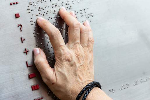 Close-up photo of a hand reading a braille map legend on a metal sign.