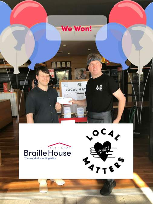 Braille House and Grill'd staff holding up a cheque in the restaurant. The photo is surrounded by balloons, and accompanied by the words: 'we won,' and the Braille House and Grill'd Local Matters logos.